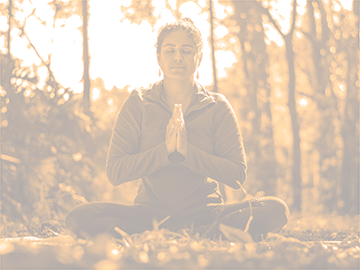 Eine Person die bei Sonnenschein im Wald meditiert.